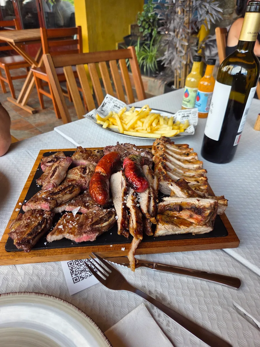 Parrillada de carne a la brasa en tabla: costillar, chuletas, entrecot y chorizo con sal gruesa, y patatas fritas al fondo