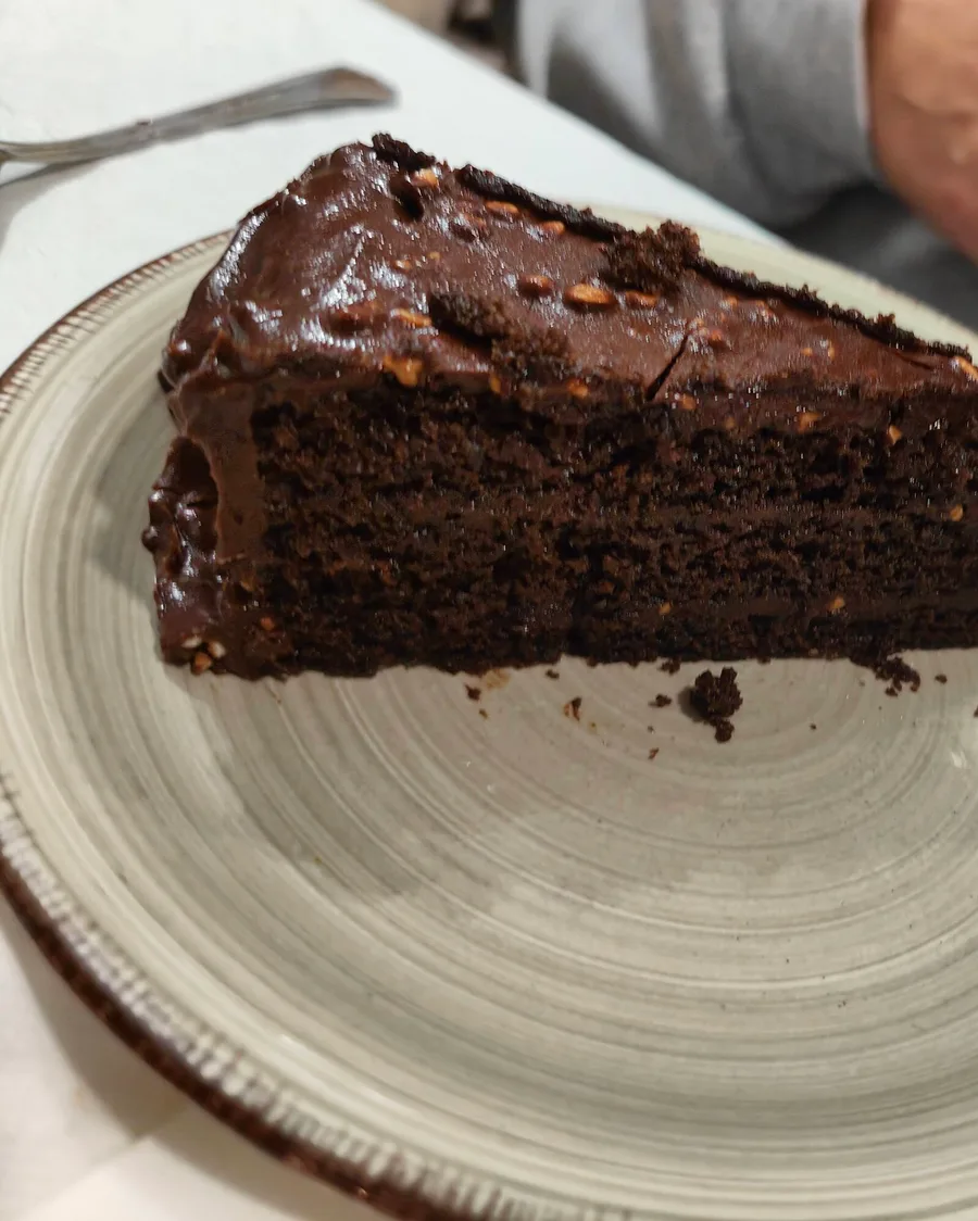 Porción de tarta de chocolate con cobertura de ganache y frutos secos, servida en plato de cerámica