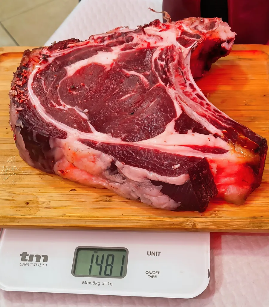 Chuletón con hueso sobre tabla de madera en una báscula que marca 1.481 gramos